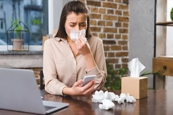 Jovem empresária usando smartphone e sofrendo de alergia no local de trabalho — Fotografia de Stock