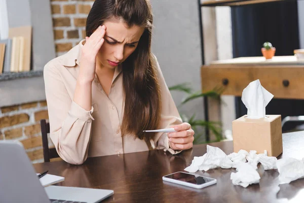 Kranke junge Geschäftsfrau hält Thermometer in der Hand und überprüft Temperatur im Büro — Stockfoto