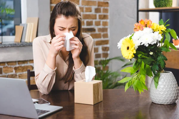 Young businesswoman blowing nose and suffering from allergy at workplace — Stock Photo