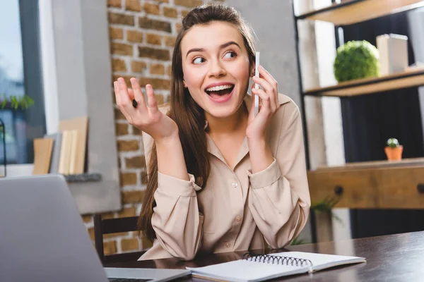 Счастливая молодая деловая женщина разговаривает по смартфону во время работы в офисе — стоковое фото