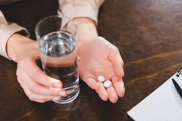 Close-up partial view of businesswoman holding pills and glass of water at workplace — Stock Photo