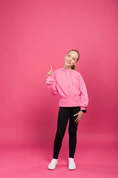 Athletic kid having idea and pointing up, isolated on pink — Stock Photo