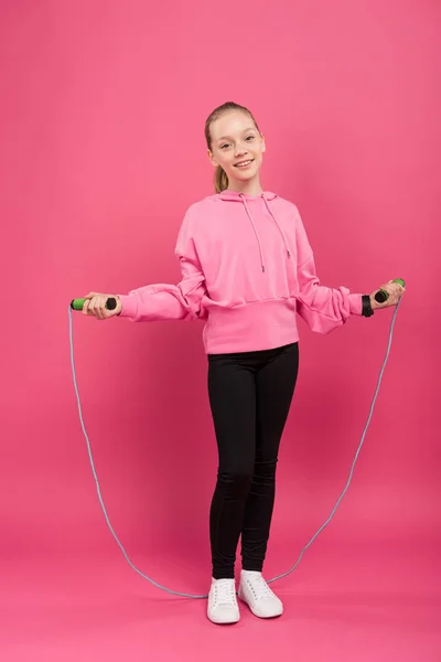 Criança bonita no treinamento de sportswear com corda de salto, isolado em rosa — Fotografia de Stock