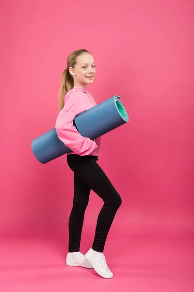 Rubia joven en ropa deportiva celebración de la alfombra de fitness, aislado en rosa - foto de stock