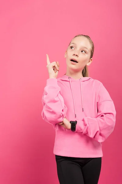 Adorable niño deportivo apuntando hacia arriba y teniendo idea, aislado en rosa - foto de stock