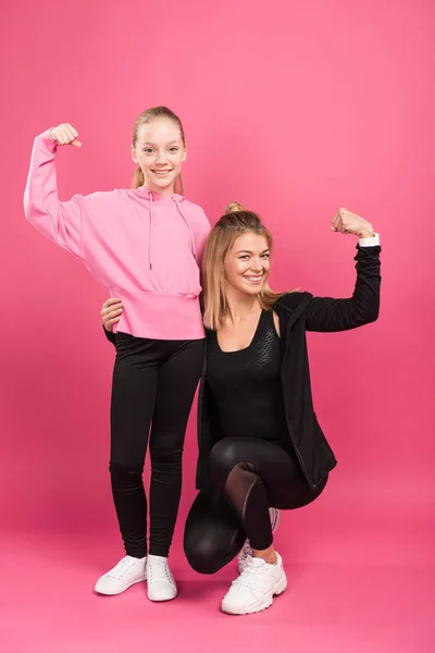Сильная мать и дочь показывают мускулистые бицепсы на розовом — стоковое фото