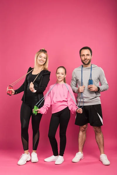 Parents and daughter in sportswear holding skipping ropes, isolated on pink — Stock Photo