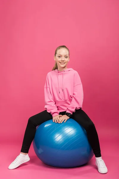 Niño deportivo sentado en pelotas de fitness, aislado en rosa - foto de stock