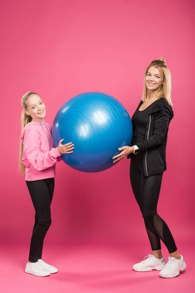 Sportliche Mutter und Tochter mit Fitnessbällen, isoliert auf rosa — Stockfoto