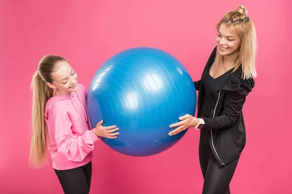 Спортивна мати і дочка тримають підходящі кульки, ізольовані на рожевому — стокове фото