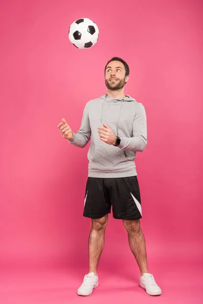 Apuesto deportista vomitando pelota de fútbol aislado en rosa - foto de stock