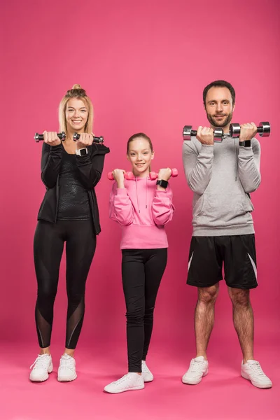 Pais esportivos e filha treinando com halteres, isolados em rosa — Fotografia de Stock