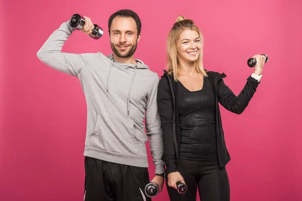 Athletic couple training with dumbbells, isolated on pink — Stock Photo
