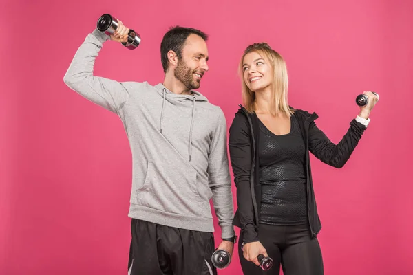 Schönes athletisches Paartraining mit Kurzhanteln, isoliert auf rosa — Stockfoto