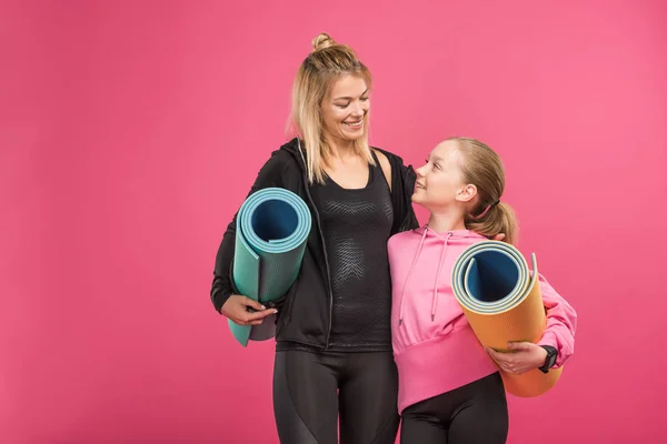 Happy mother and sporty daughter holding fitness mats, isolated on pink — Stock Photo