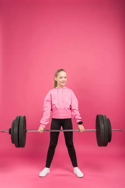 Sportive youngster exercising with barbell, isolated on pink — Stock Photo