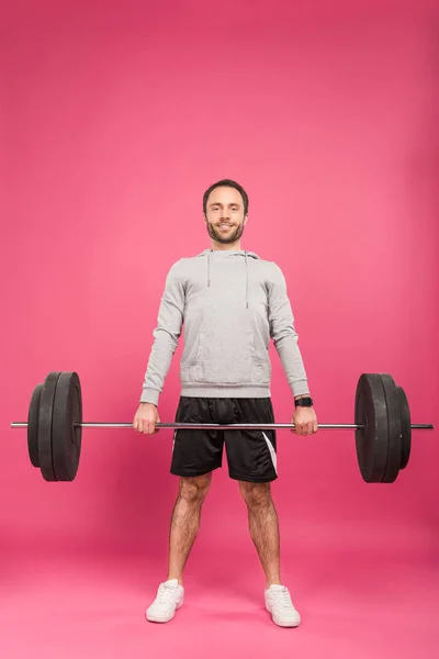 Athletic man in sportswear training with barbell, isolated on pink — Stock Photo