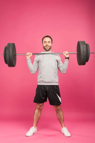 Handsome sportsman exercising with barbell, isolated on pink — Stock Photo