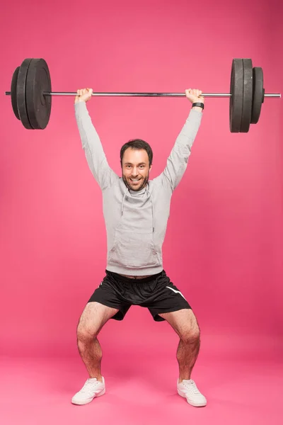 Strong sportsman training with barbell, isolated on pink — Stock Photo
