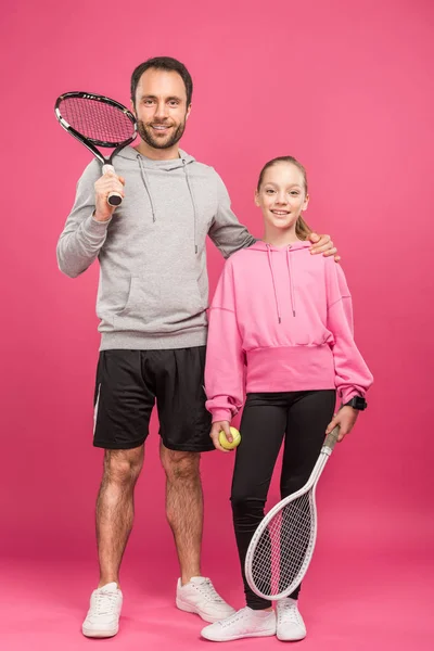 Schöner Vater und Tochter mit Tennisschlägern und Ball, isoliert auf rosa — Stockfoto