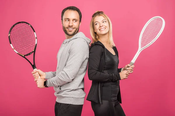 Feliz pareja atlética sosteniendo raquetas de tenis, aislado en rosa - foto de stock