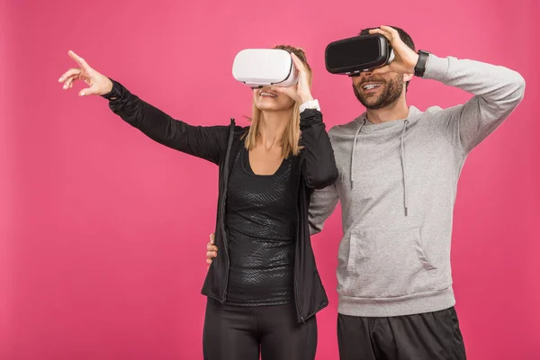 Pareja haciendo gestos y usando auriculares de realidad virtual, aislados en rosa - foto de stock