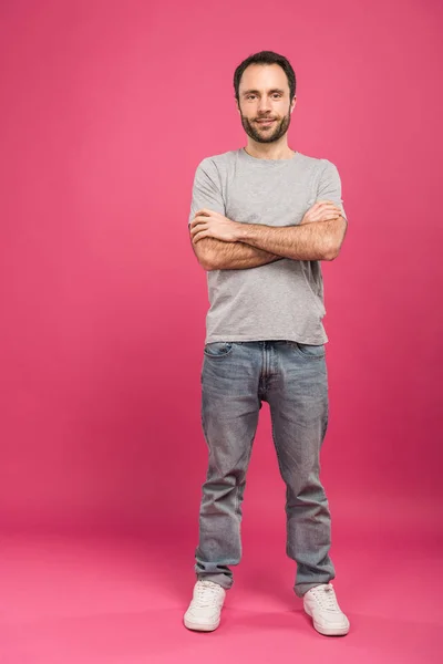 Feliz hombre guapo posando con los brazos cruzados, en rosa - foto de stock