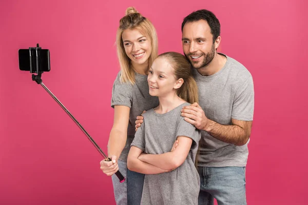 Hermosa familia feliz tomando selfie en el teléfono inteligente, aislado en rosa - foto de stock
