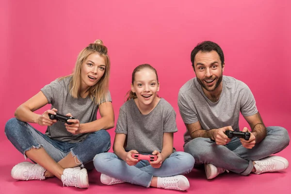 Aufgeregte Familie spielt Videospiel mit Joysticks, isoliert auf rosa — Stockfoto