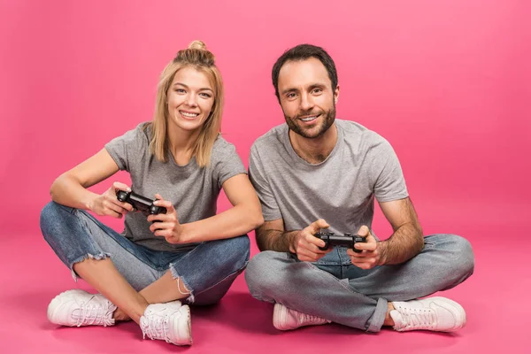 Beautiful smiling couple playing video game with joysticks, isolated on pink — Stock Photo