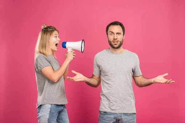 Mulher zangada gritando com megafone em homem confuso com gesto de encolher os ombros, isolado em rosa — Stock Photo