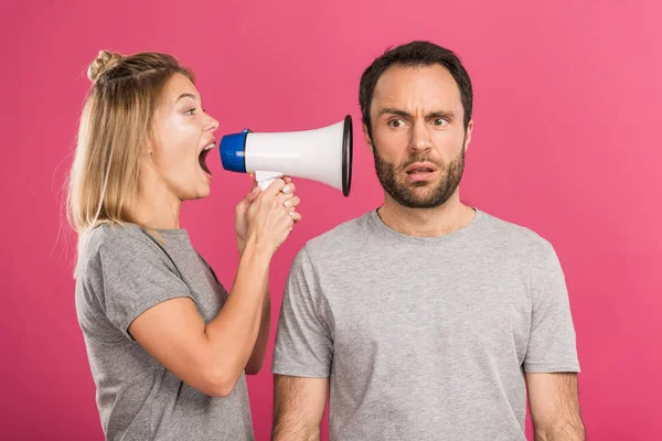 Beautiful angry woman screaming with megaphone at confused man, isolated on pink — Stock Photo