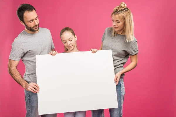 Сім'я позує з порожнім плакатом, ізольована на рожевому — стокове фото