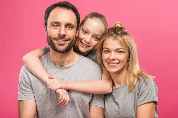 Lächelnde Tochter umarmt ihre glücklichen Eltern, isoliert auf rosa — Stockfoto