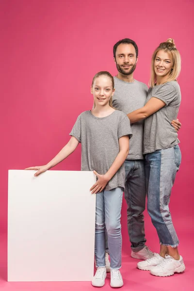 Hermosa familia posando con cartel vacío, aislado en rosa - foto de stock
