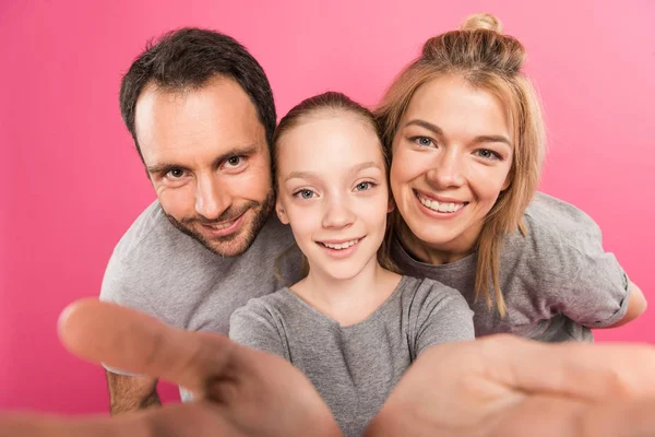 Feliz hija y sonrientes padres tomando selfie juntos, aislado en rosa - foto de stock