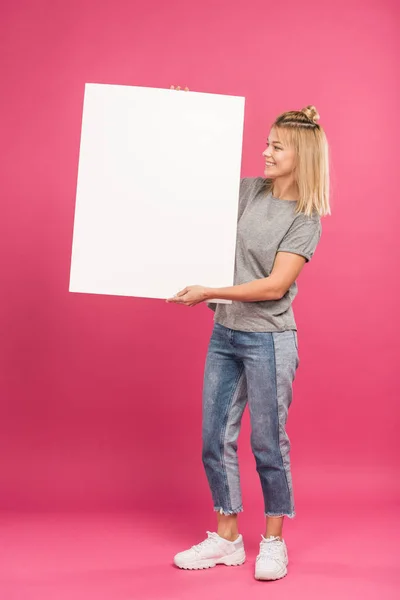Hermosa mujer feliz posando con cartel vacío, aislado en rosa - foto de stock