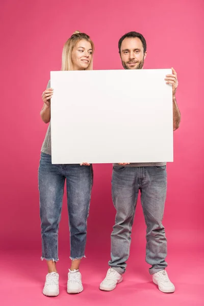 Sonriente pareja posando con la tarjeta vacía, aislado en rosa - foto de stock