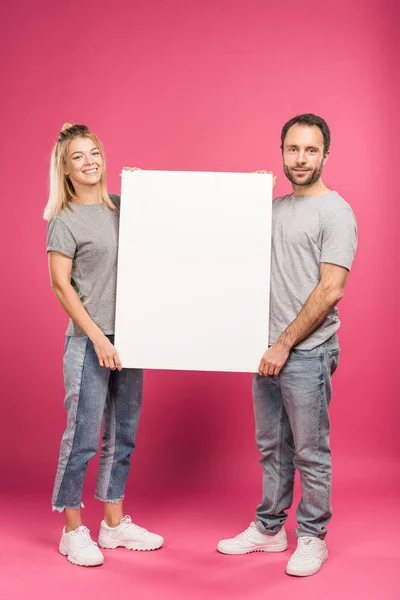 Beautiful couple posing with empty board, isolated on pink — Stock Photo