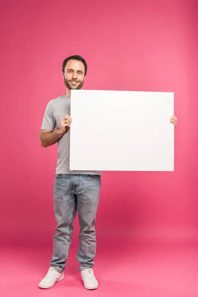 Schöner lächelnder Mann posiert mit leerem Brett, isoliert auf rosa — Stockfoto
