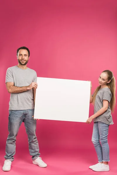 Hermoso padre e hija posando con pancarta en blanco, aislado en rosa - foto de stock