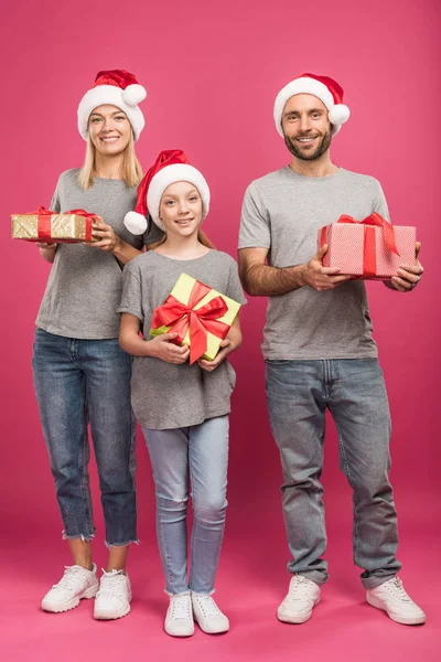 Happy family in santa hats holding christmas gift boxes on pink — Stock Photo