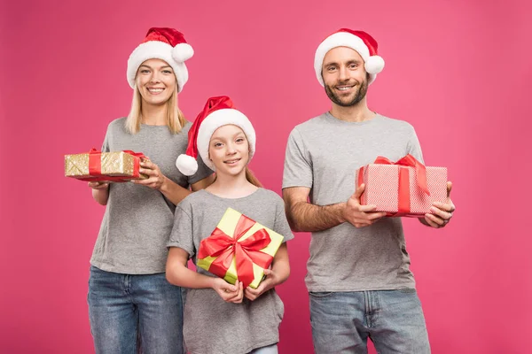 Figlia sorridente e regali in cappelli di Babbo Natale tenendo regali di Natale isolati su rosa — Foto stock
