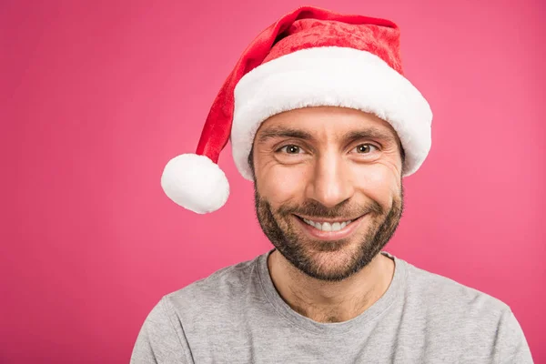 Ritratto di bell'uomo sorridente in cappello di Babbo Natale, isolato su rosa — Foto stock