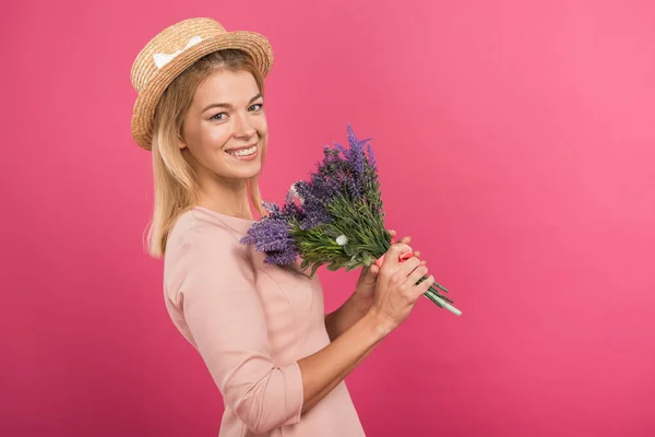 Bella donna sorridente in posa in cappello di paglia con bouquet di fiori, isolato su rosa — Foto stock