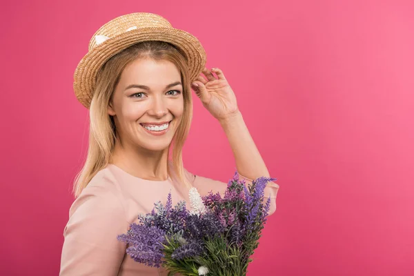 Красива щаслива жінка позує в солом'яному капелюсі з букетом квітів, ізольована на рожевому — стокове фото