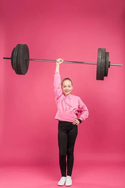 Athletic youngster training with barbell, isolated on pink — Stock Photo