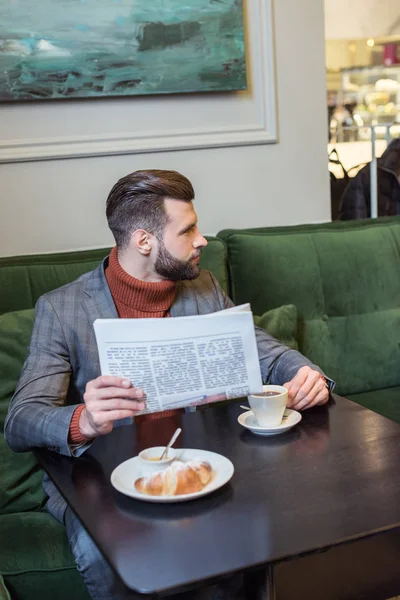 Homem elegante bonito no desgaste formal sentado à mesa durante o almoço e ler jornal no restaurante — Fotografia de Stock