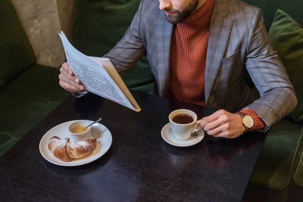 Обрезанный вид стильного мужчины в формальной одежде, сидящего за столом и читающего газету в ресторане — стоковое фото
