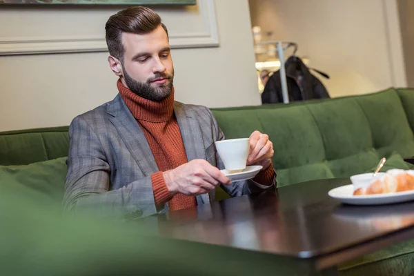 Messa a fuoco selettiva di bell'uomo in abito formale seduto a tavola e bere caffè nel ristorante — Foto stock